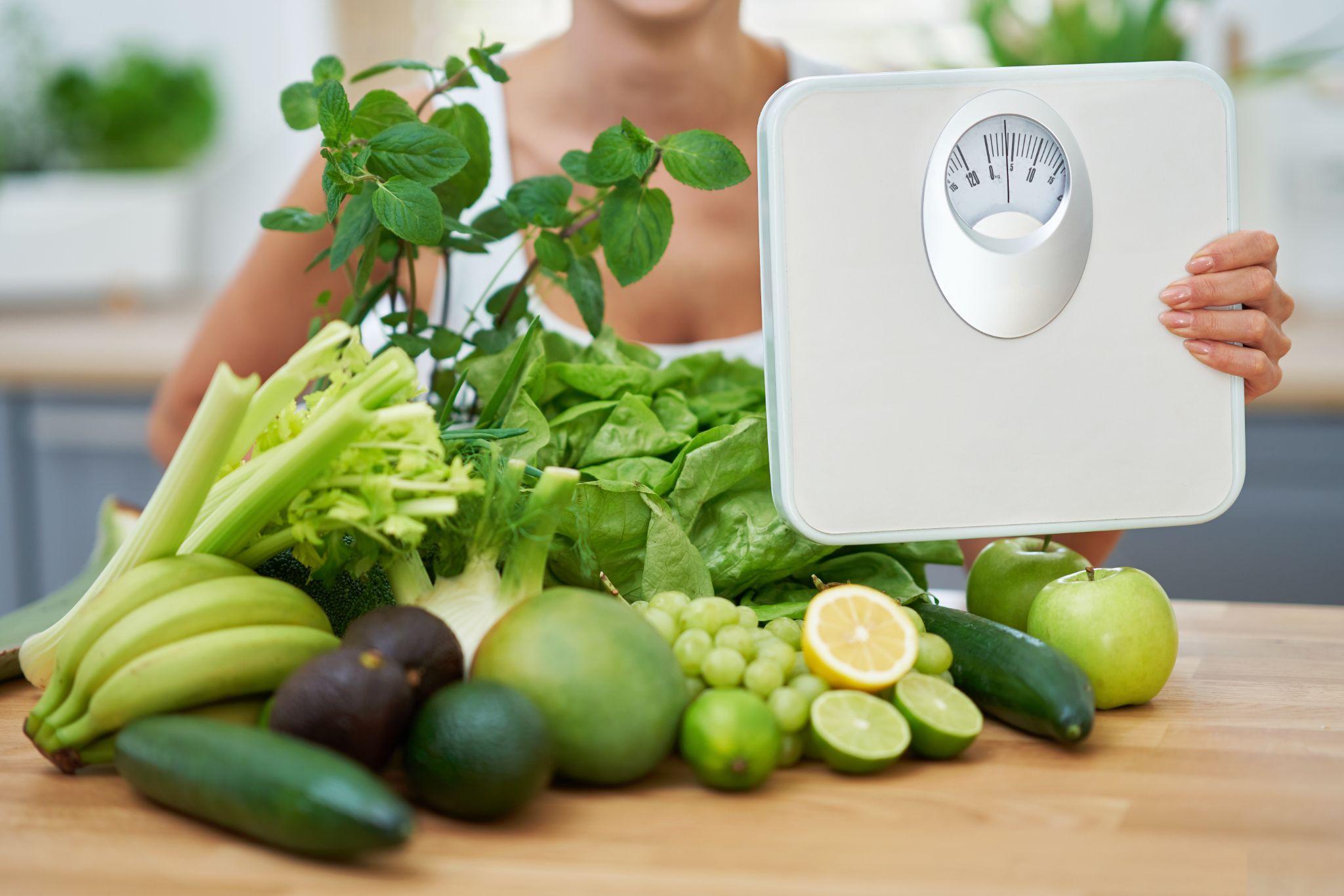 woman with weighing scale and assorted fruits and vegetables