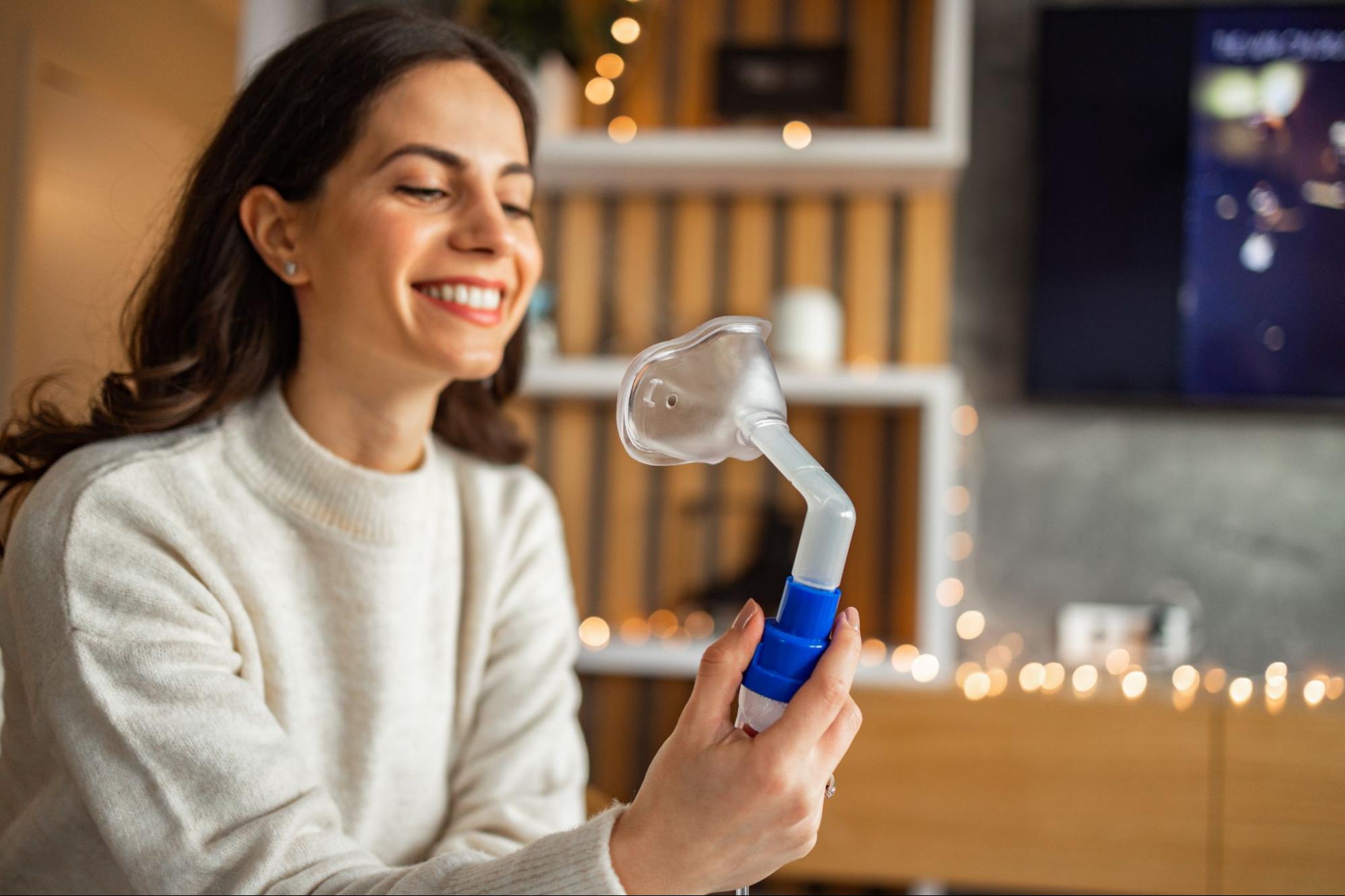 Woman holding a nasal CPAP mask at home, preparing to adjust the fit for comfortable sleep therapy.