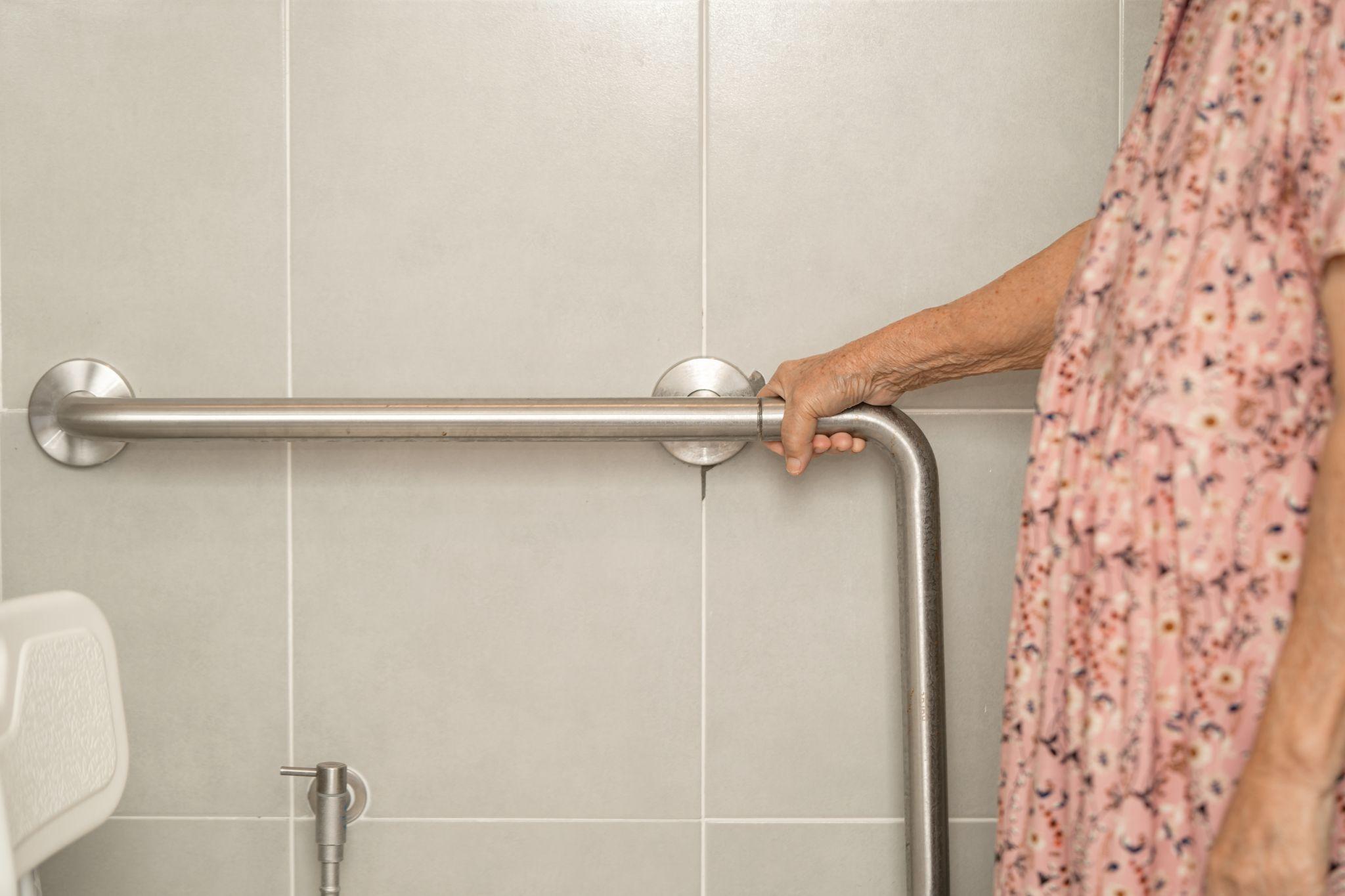 elderly woman using grab bars in a bathroom, representing the importance of knowing the answer to the question “What are the best bathroom safety products to prevent falls at home?”