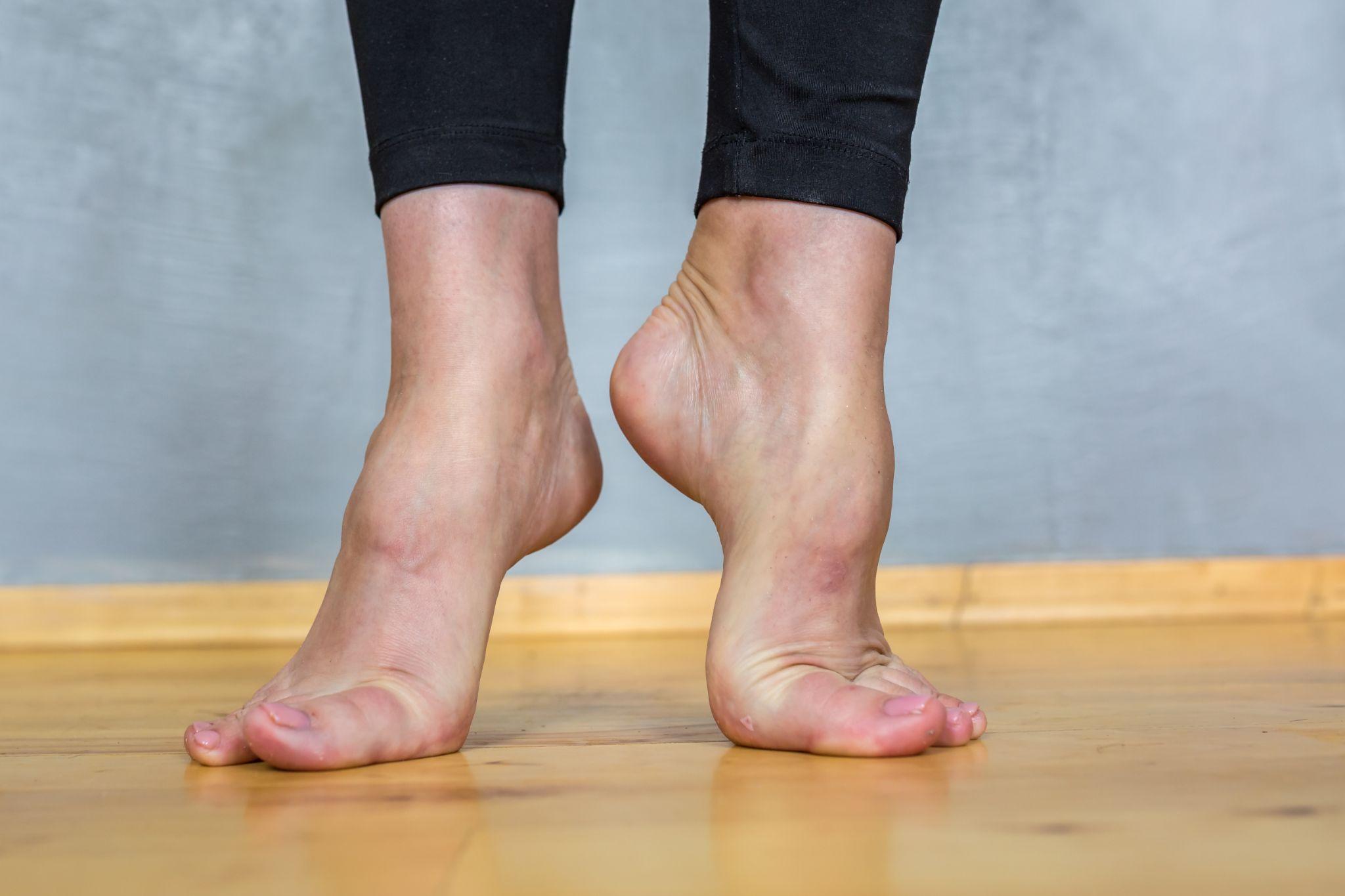 woman standing barefoot on a wooden floor, showing foot arches and the need for proper arch support