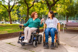 Two women using wheelchairs talking in a park, representing mobility equipment available through a medical supply company.