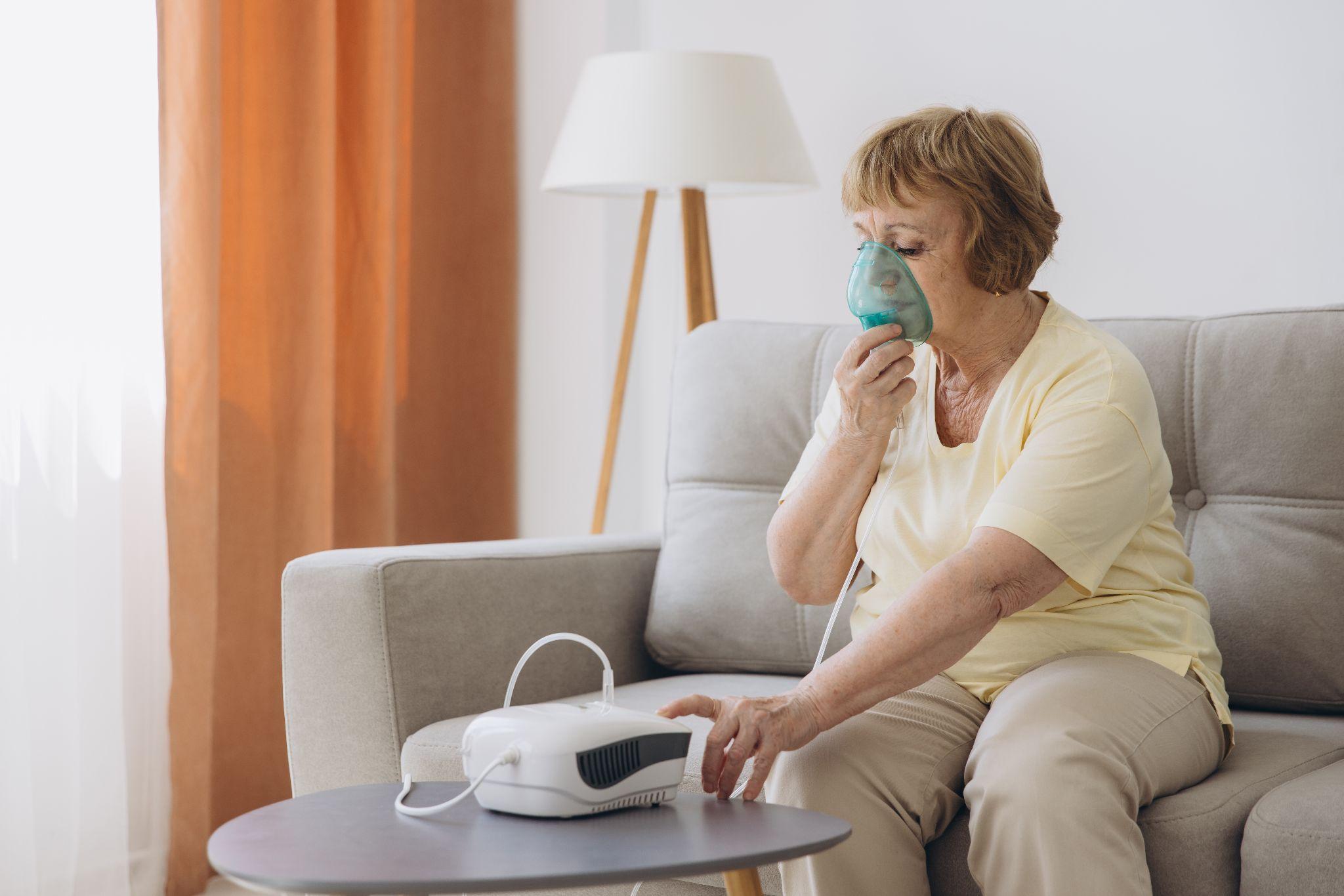 Senior woman using a nebulizer at home, showing respiratory equipment for daily treatment and home medical care
