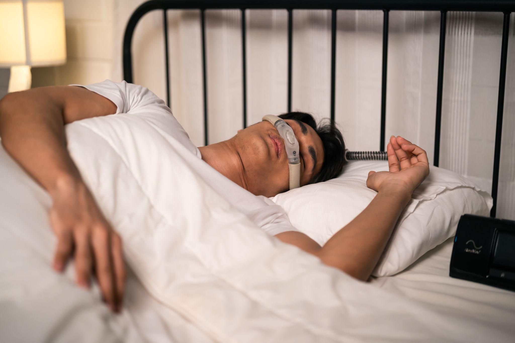 Man sleeping with a CPAP machine, representing home respiratory equipment for sleep apnea treatment and daily care