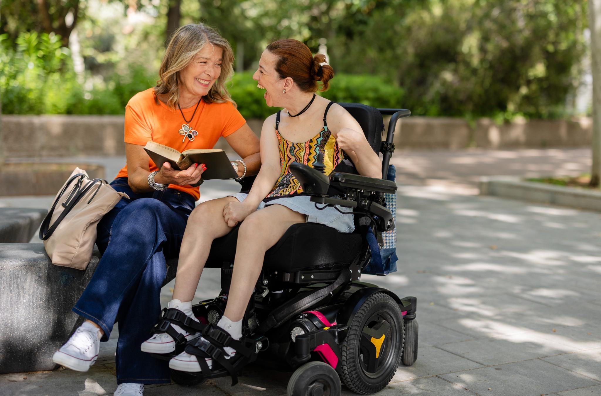 Caregiver and woman in wheelchair smiling outdoors