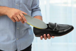 Person placing a custom orthotic insert into a black dress shoe for custom orthotics in the RGV.