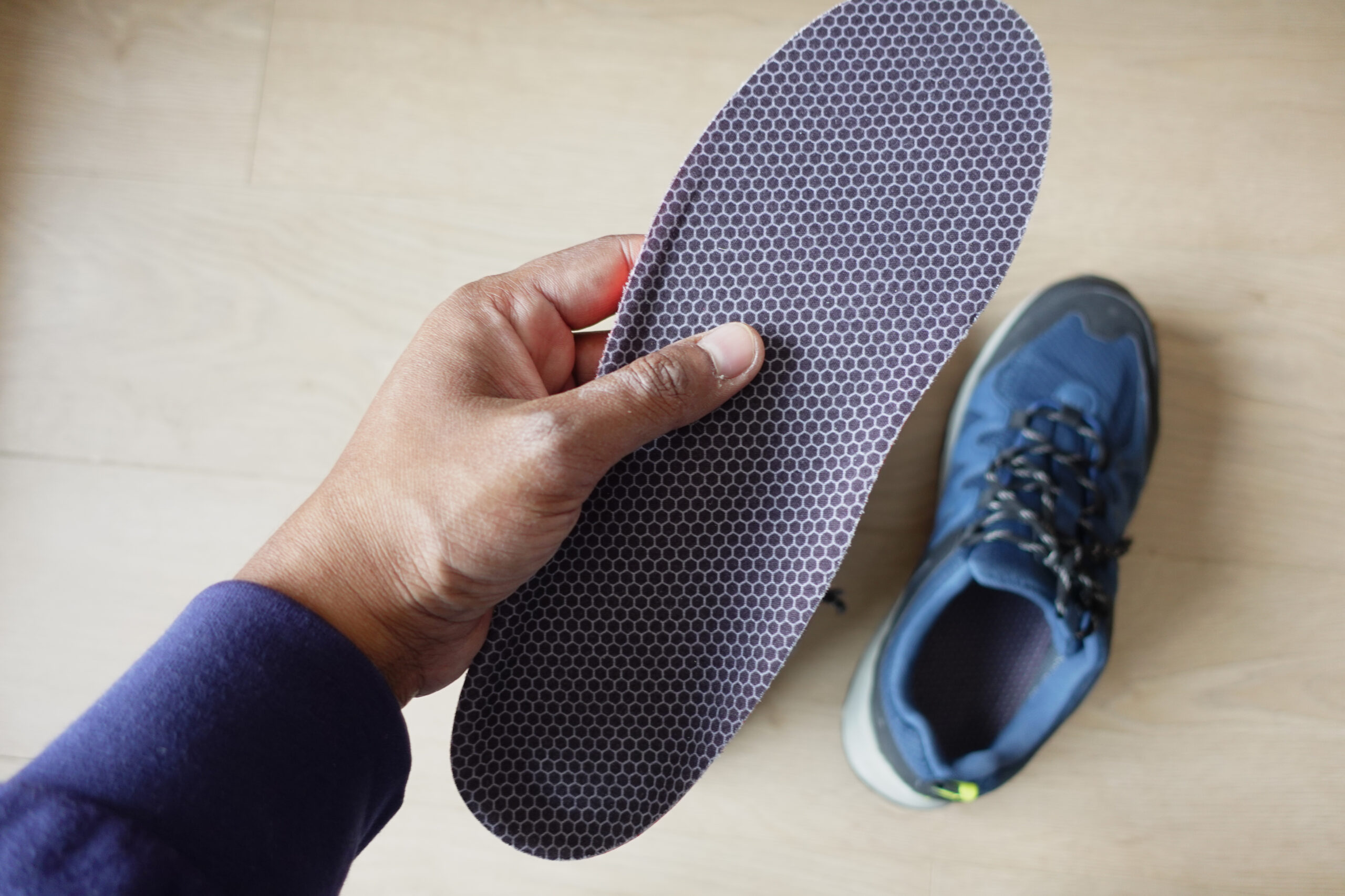 Hand holding a custom orthotic insole beside a sneaker