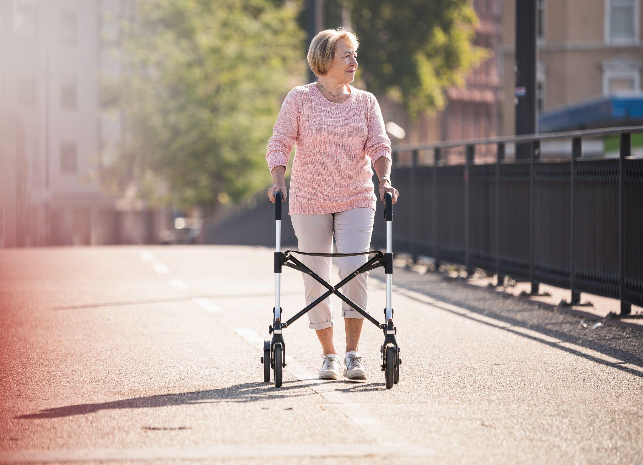 Elderly woman walking with a rollator walker outdoors, highlighting durable medical equipment for daily mobility