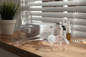Nebulizer with face mask and medications on wooden table indoors. Inhalation equipment