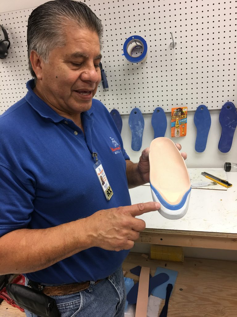 A technician holding a handcrafted blue and beige shoe insert during custom orthotic fabrication in South Texas at MacPherson's Medical Supply.