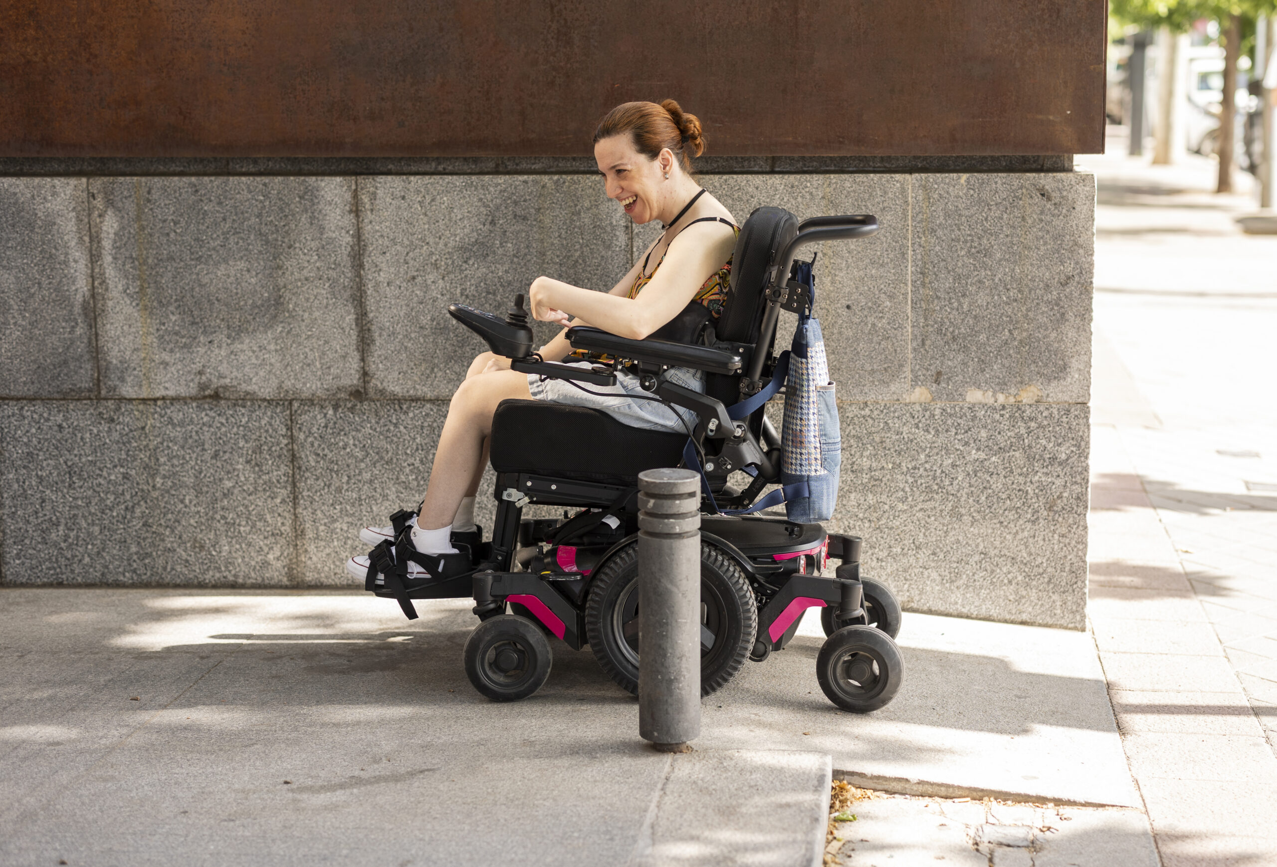 A smiling woman navigating a city sidewalk in her motorized wheelchair, representative of daily independence supported by a CRT provider