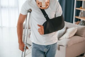 Man wearing a shoulder immobilizer while sitting on a sofa during recovery at home.