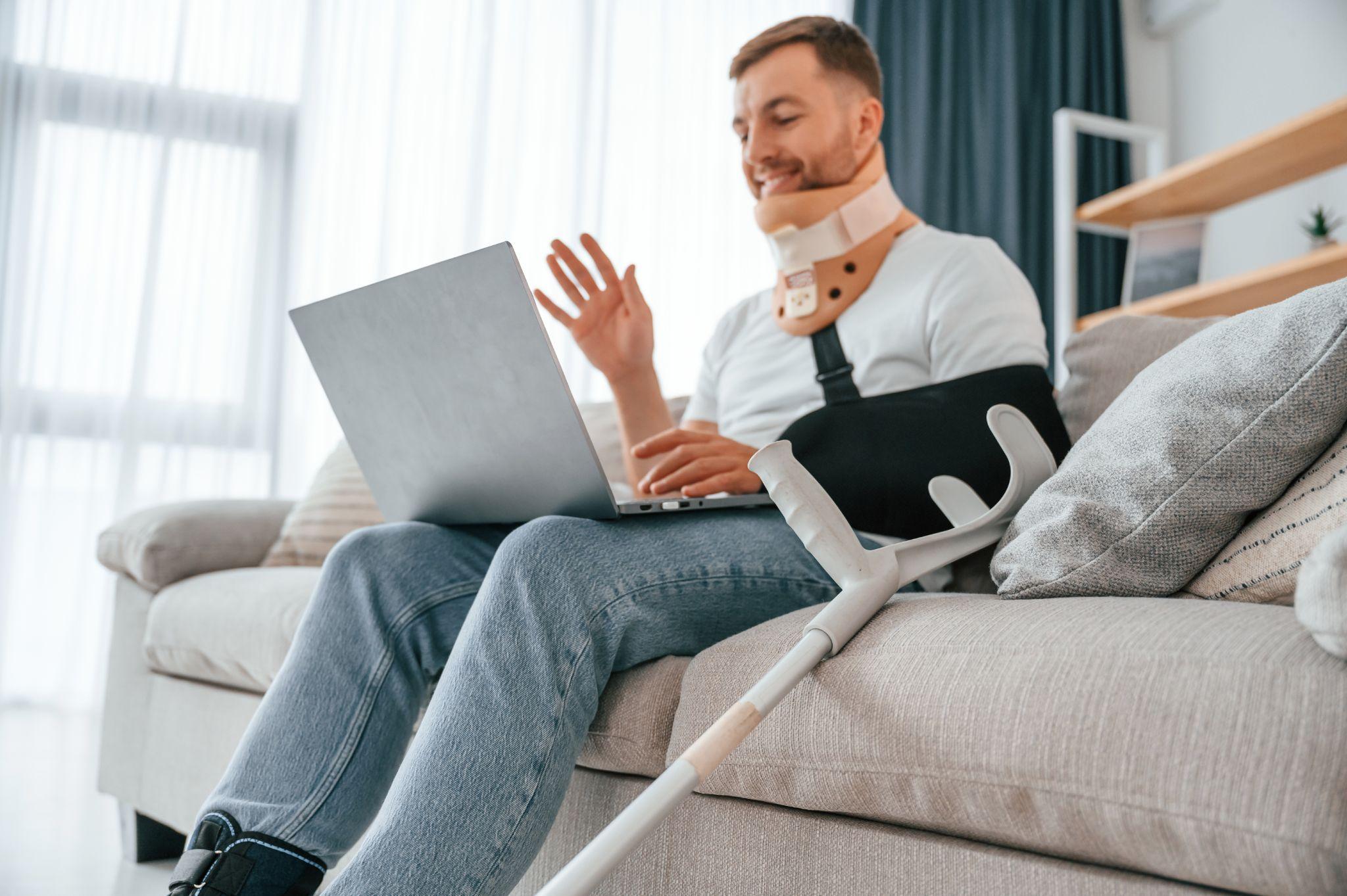 Man wearing a shoulder immobilizer while using a laptop during recovery at home.