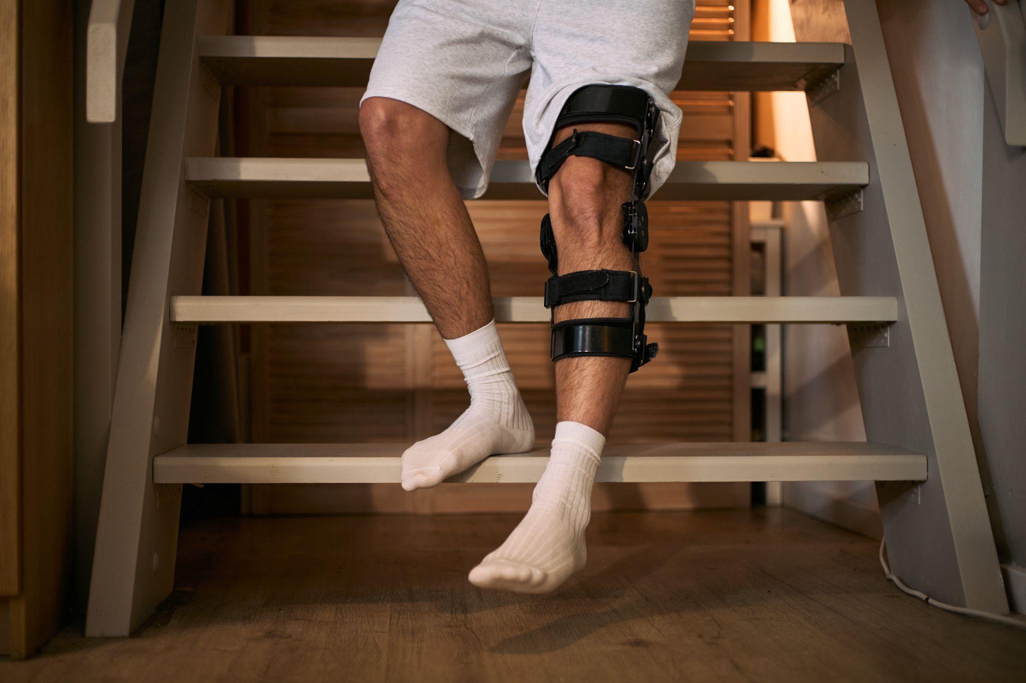 Man wearing an orthopedic knee brace while carefully navigating stairs during recovery at home.