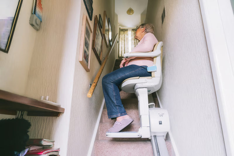 Older adult using a stair lift at home as part of an accessible mobility setup alongside patient lift solutions.