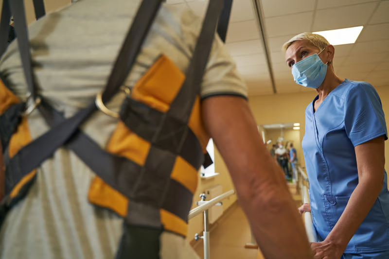 Caregiver assisting a person wearing a patient lift sling during mobility and transfer support.