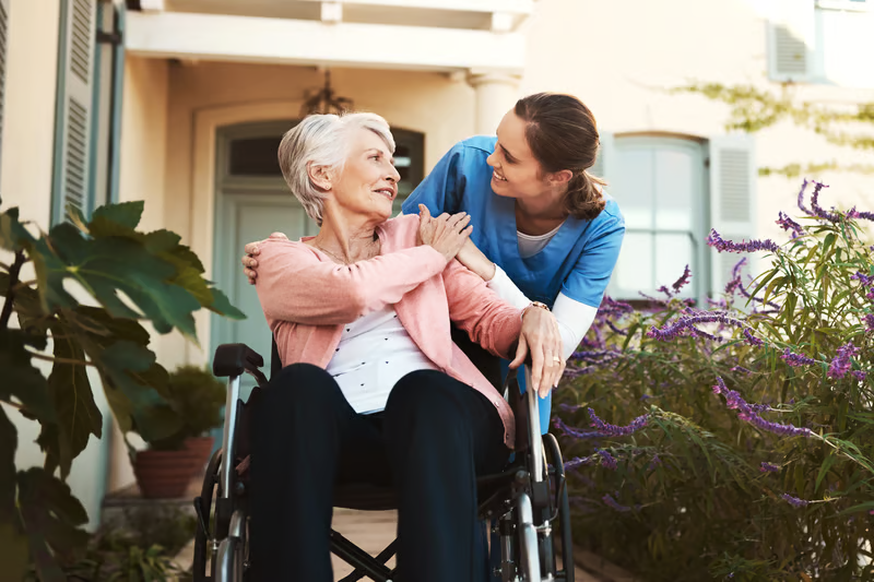 Caregiver assisting an older adult in a wheelchair outside her home, showing how home care equipment can support mobility and independence.