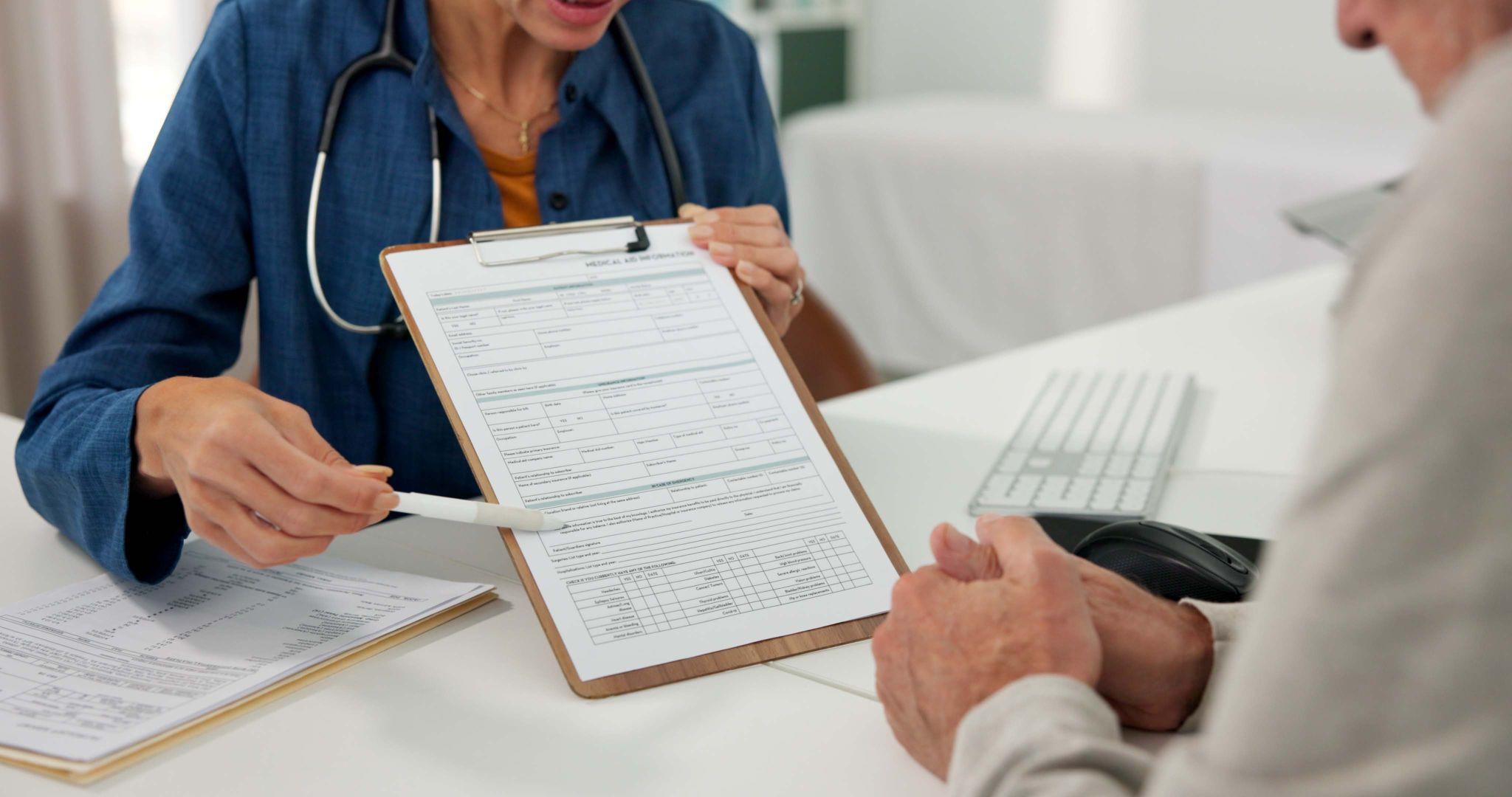 Medical professional reviewing paperwork with an older patient during a consultation.